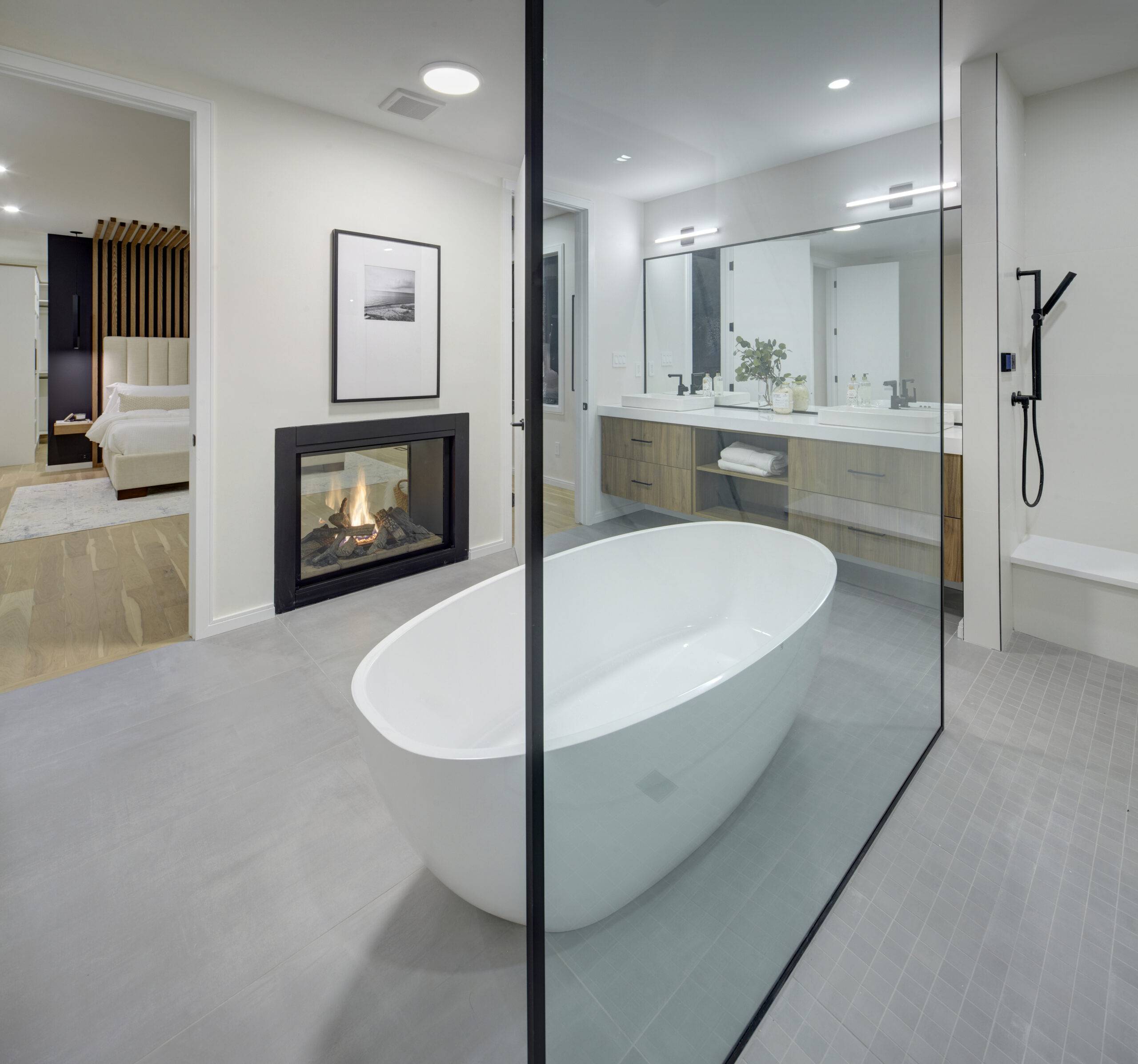 A modern bathroom with white marble tile walls, a freestanding bathtub, a glass shower enclosure, and dual sinks with a wooden vanity.