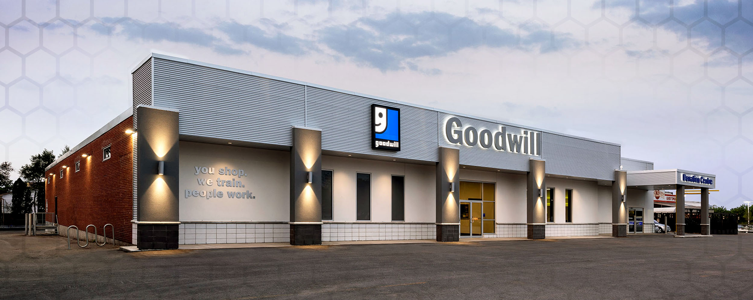 Commercial construction project, the Front of Goodwill store, London, Ontario which has 5 grey columns with lights, white exterior walls and the Goodwill Sign above the front door. There is a drive through area at the side of the building for donations to be dropped off.