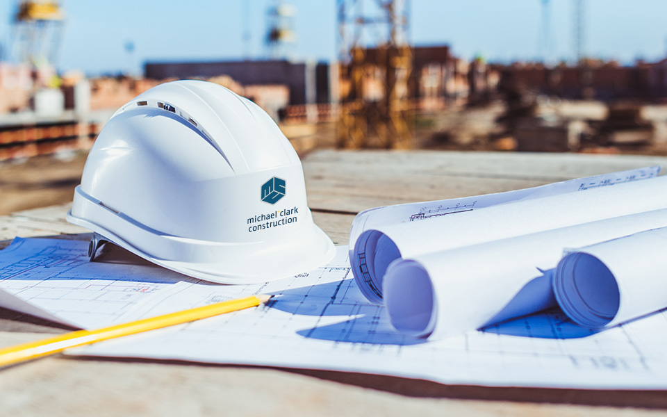 Construction Safety hat with michael + clark logo sitting on top of construction drawing.