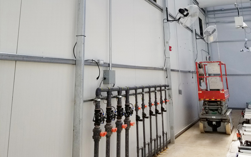 WeedMD, Interior photo showing pipes with shutoff levers on them, a sissor jack against the wall and fans hanging on the wall