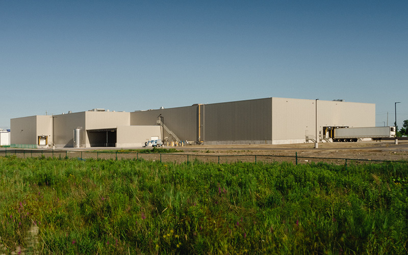 Exterior view of Frulact building, beige metal building with shipping docks and covered loading area.