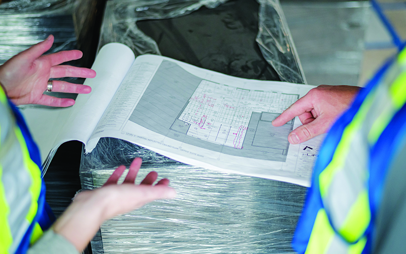 two construction workers, discussing a blueprint of a building.