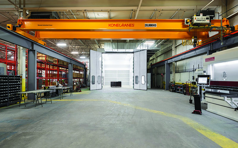 Interior Photo of Spark Power warehouse area with a large orange overhead crane in the center and concrete floor underneath.