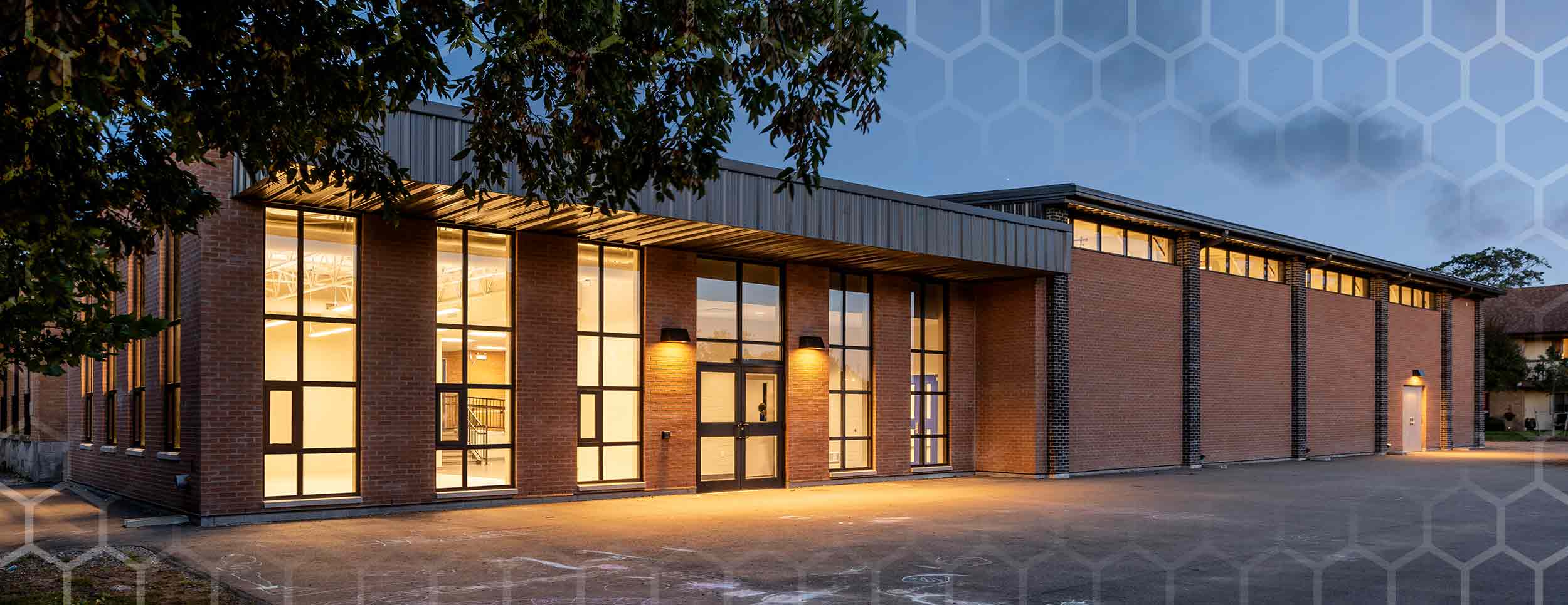 Covenant School, exterior evening photo showing front of the building with an interior room to the left lit up through the windows. Brown Brick facade and black window outlines