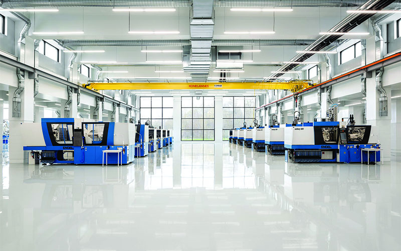 Starlim production room, open concept, white floor, walls and ceilings with automated machines down the left and right. Full wall of 12 windows in a rectangle pattern.