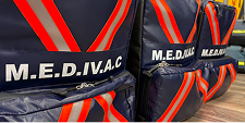 Close-up of three navy blue MEDIVAC bags with bold red-and-orange stripes, displaying the acronym M.E.D.I.V.A.C., resting on a wooden floor.